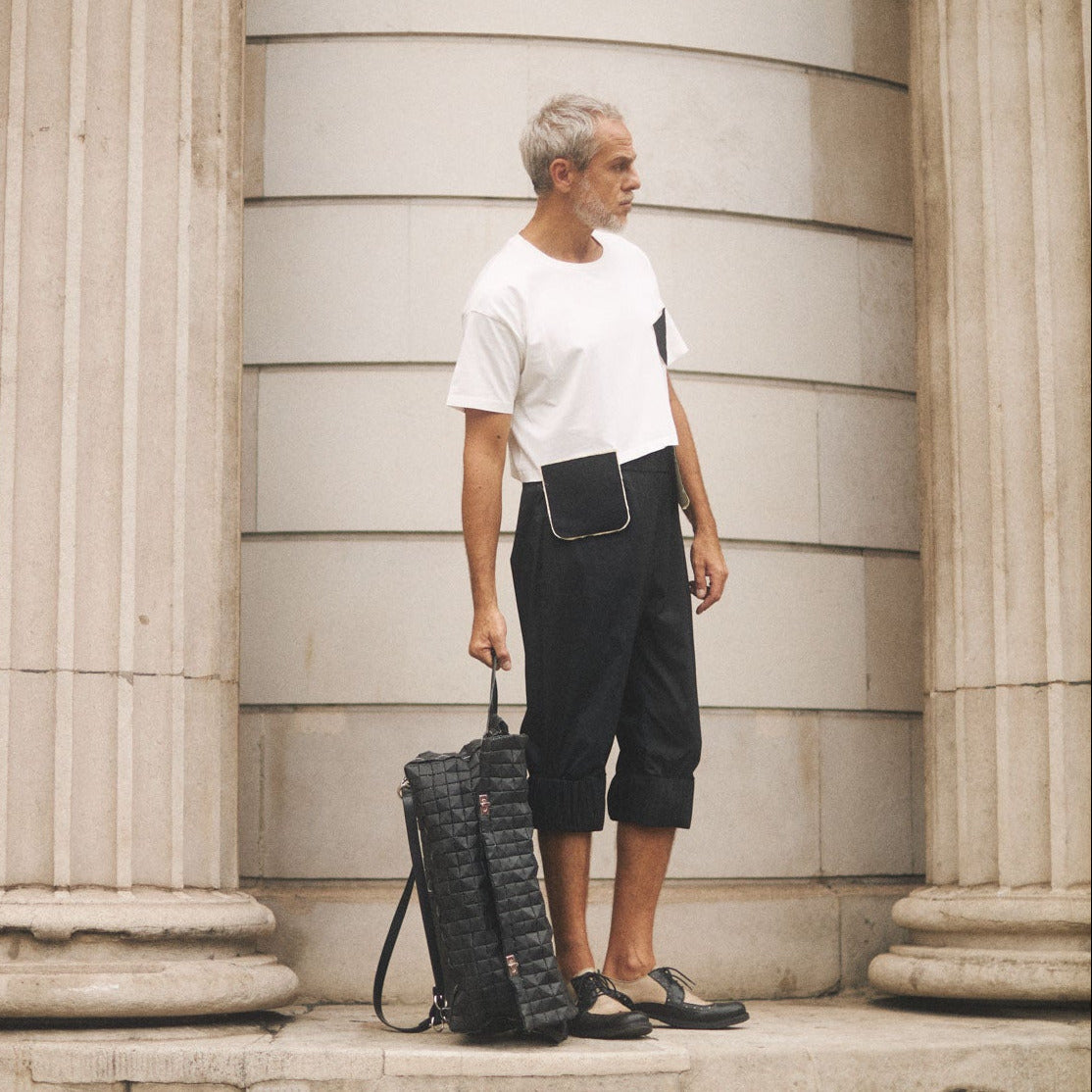Man standing against a classical building with columns, holding a travelbag.